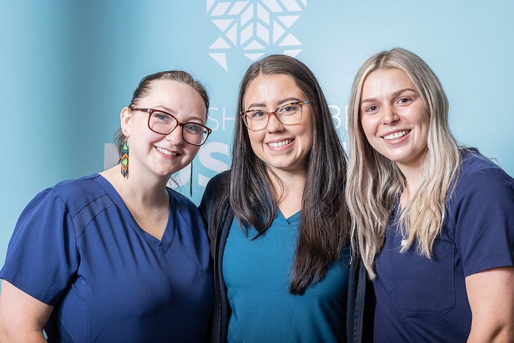 Three female medical staff members smiling in scrubs at healthcare facility