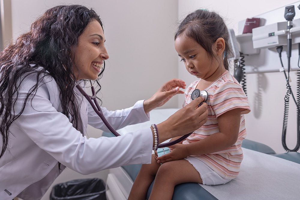 Physician examining young Indigenous child with stethoscope in examination room