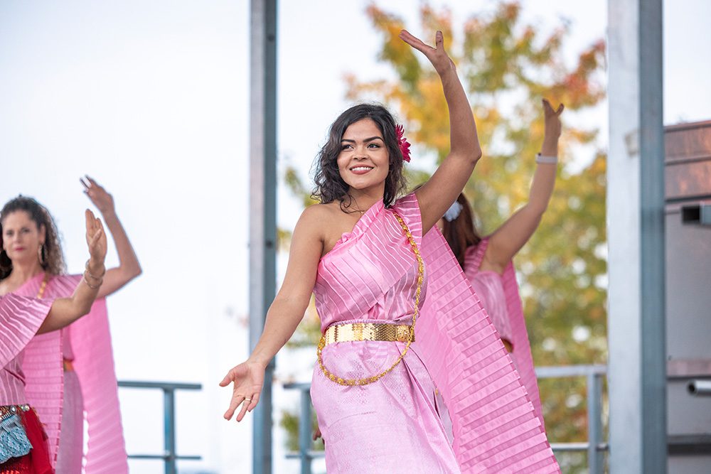 Young belly dancer in pink costume performing with raised arms