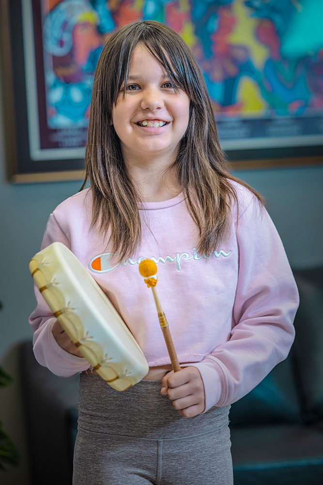 Young Indigenous girl smiling while holding traditional hand drum at Anishnawbe Mushkiki cultural center