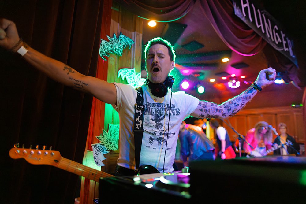 Tattooed DJ with headphones energetically performing with arms raised