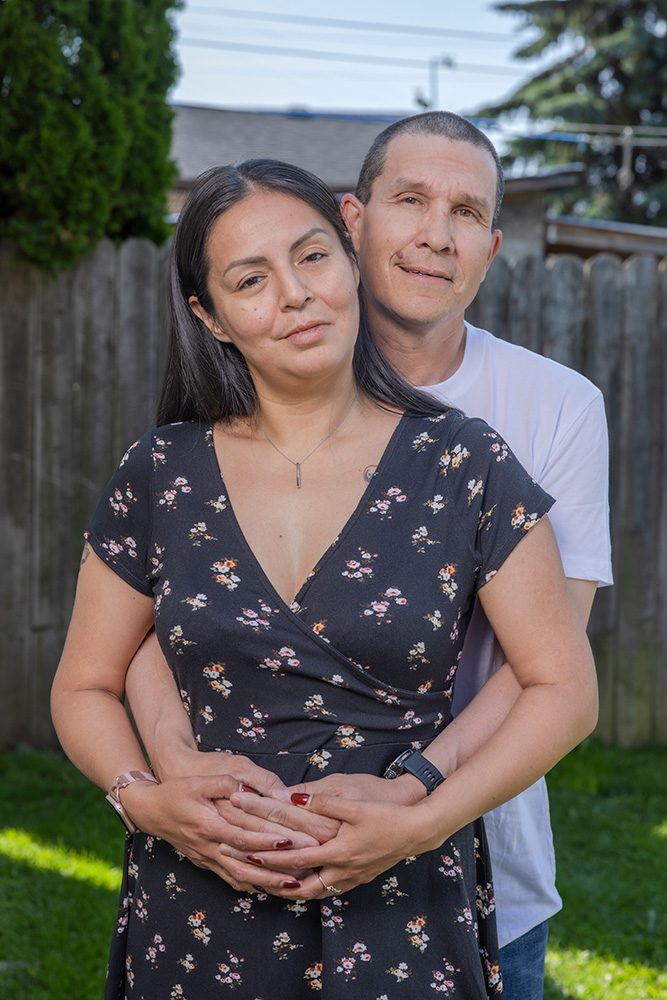 Couple standing together in backyard with woman in front wearing black floral dress