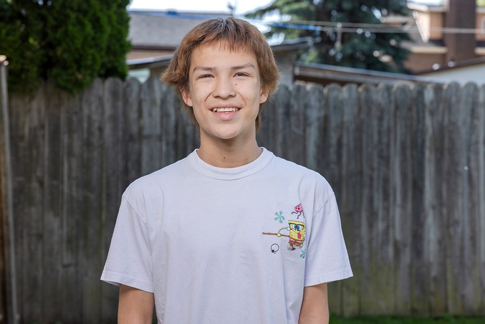 Smiling teenage boy with short brown hair wearing white SpongeBob t-shirt in backyard