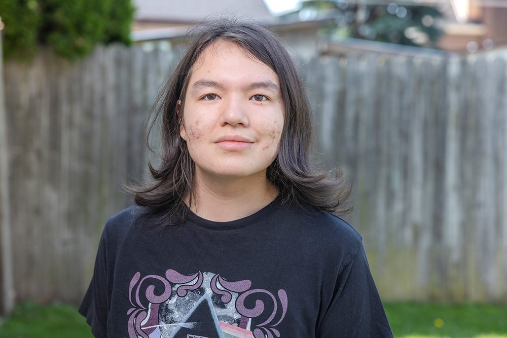 Young person with shoulder-length dark hair in black graphic t-shirt in backyard setting