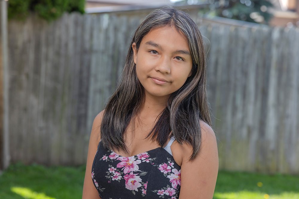 Young girl with long dark hair in black floral tank top standing in backyard