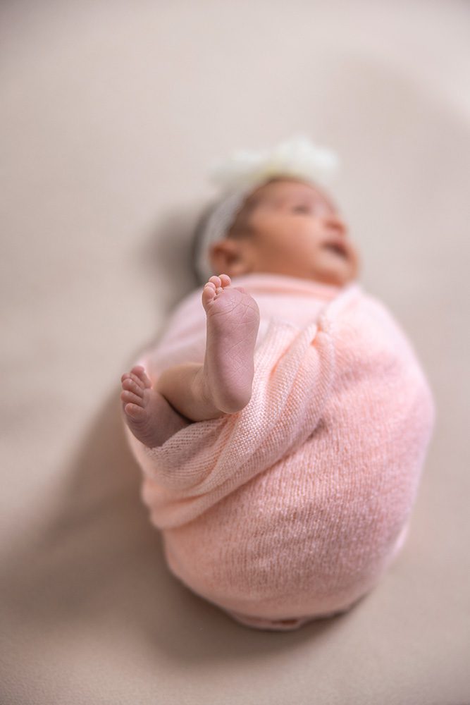 Newborn baby in pink wrap with focus on tiny feet peeking out on beige background