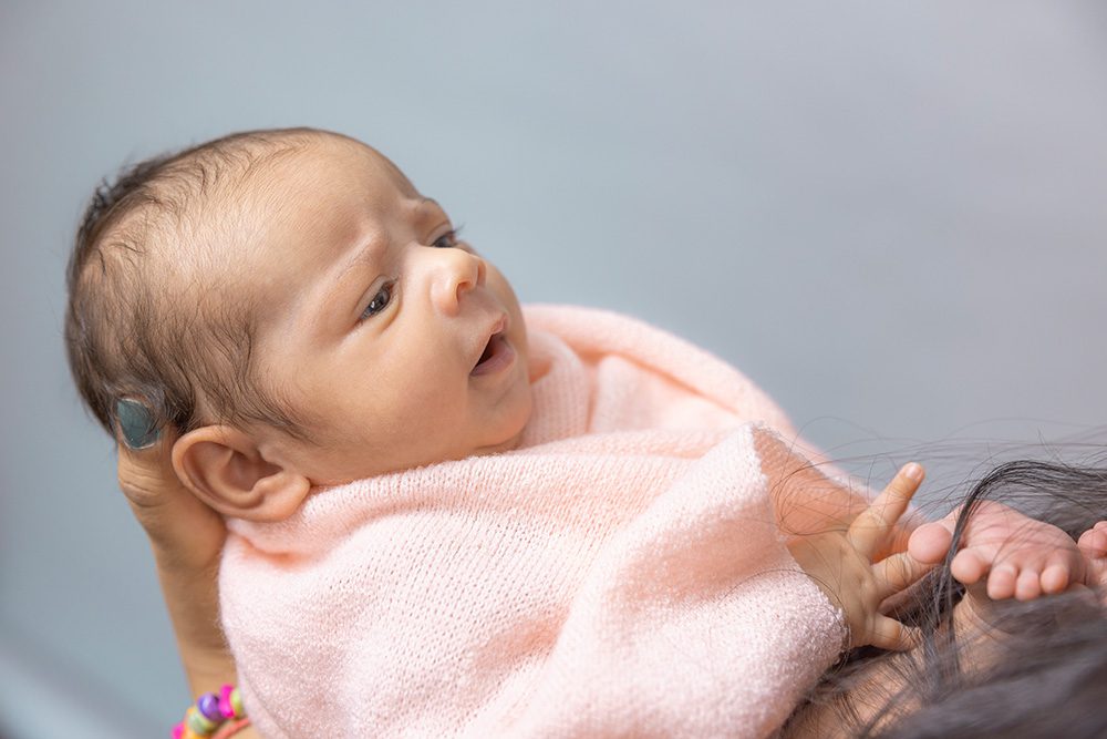 Newborn baby in pink wrap lying on parent's chest looking upward