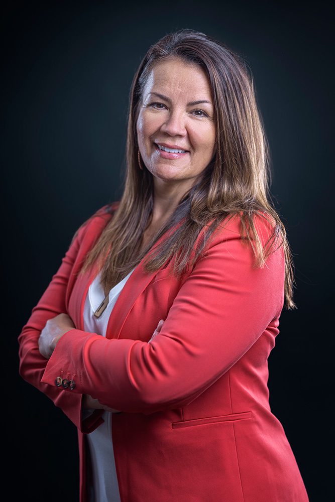 Professional business portrait of woman in coral suit with arms crossed turned slightly to side
