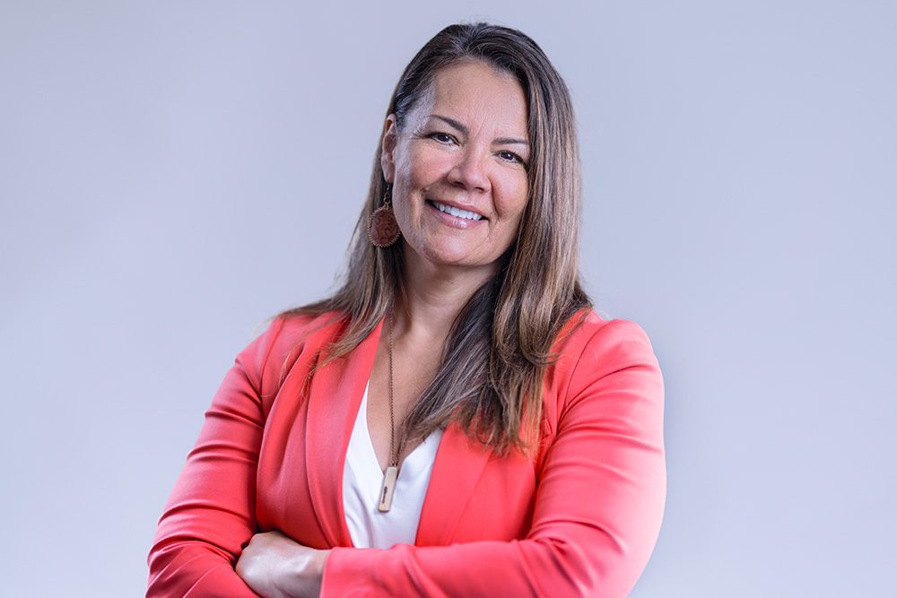 Business professional in coral blazer against light gray background with arms crossed