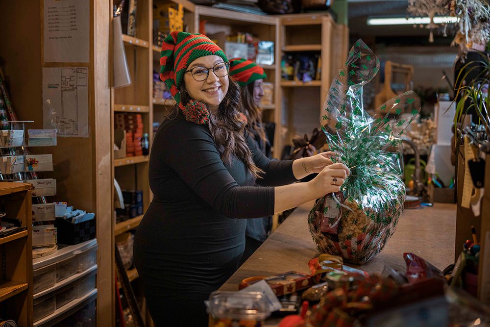 Woman in elf hat wrapping large holiday gift basket at retail counter