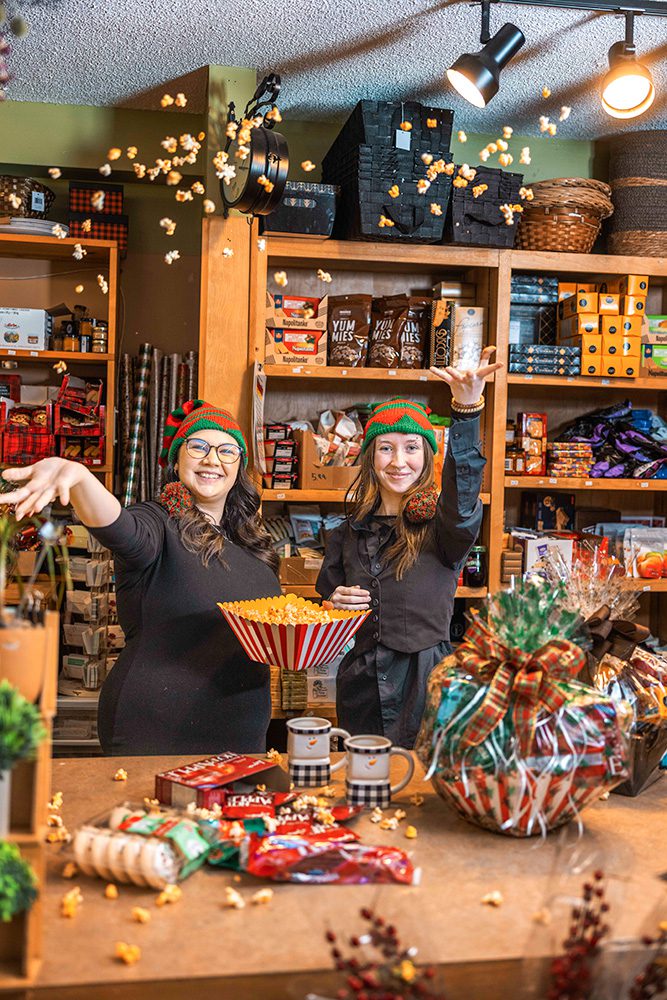 Two women in elf hats behind counter with popcorn bowl and holiday products at Georges Market