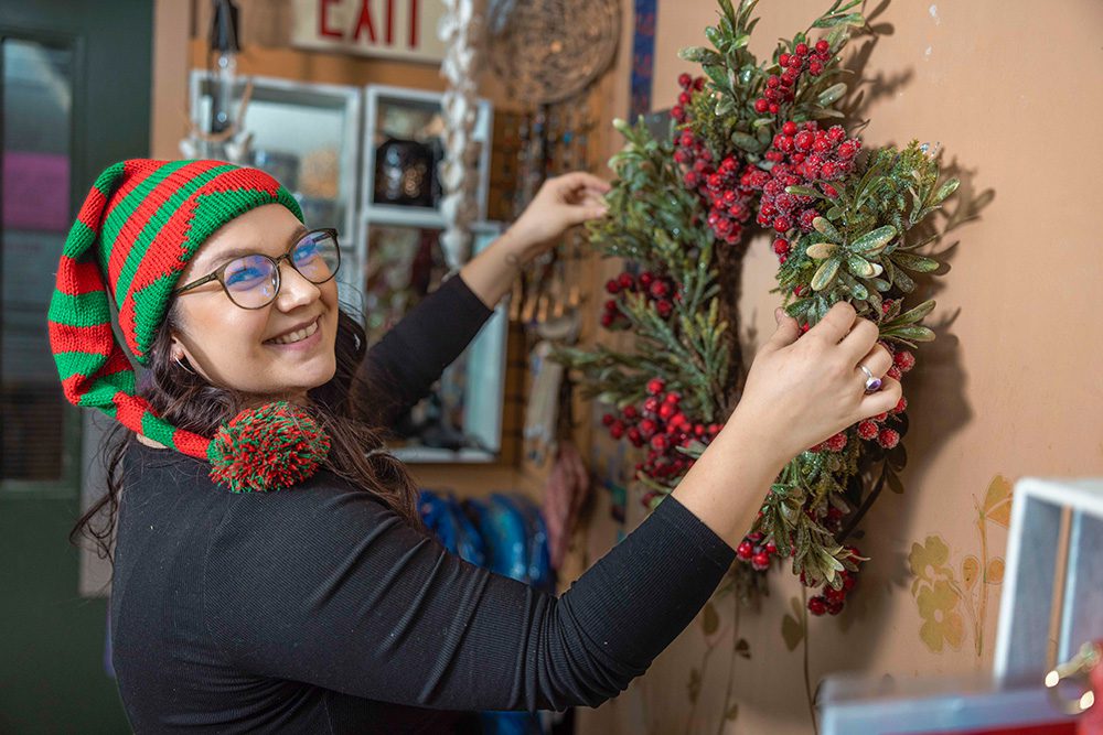 Young woman in red and green striped elf hat arranging evergreen wreath with red berries