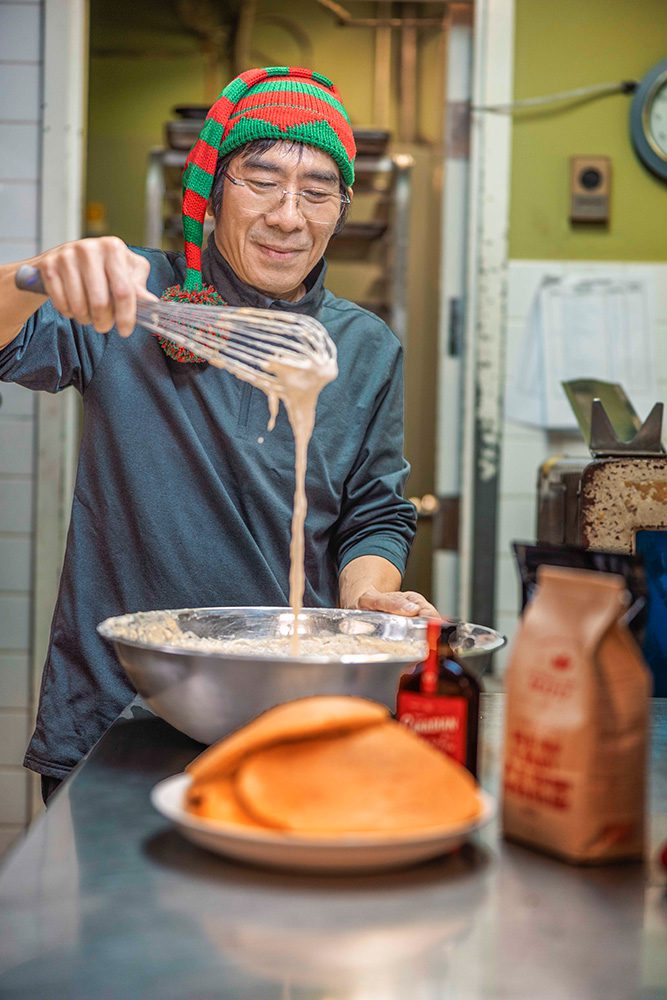 Person in red and green striped elf hat whisking batter in commercial kitchen during holiday photoshoot