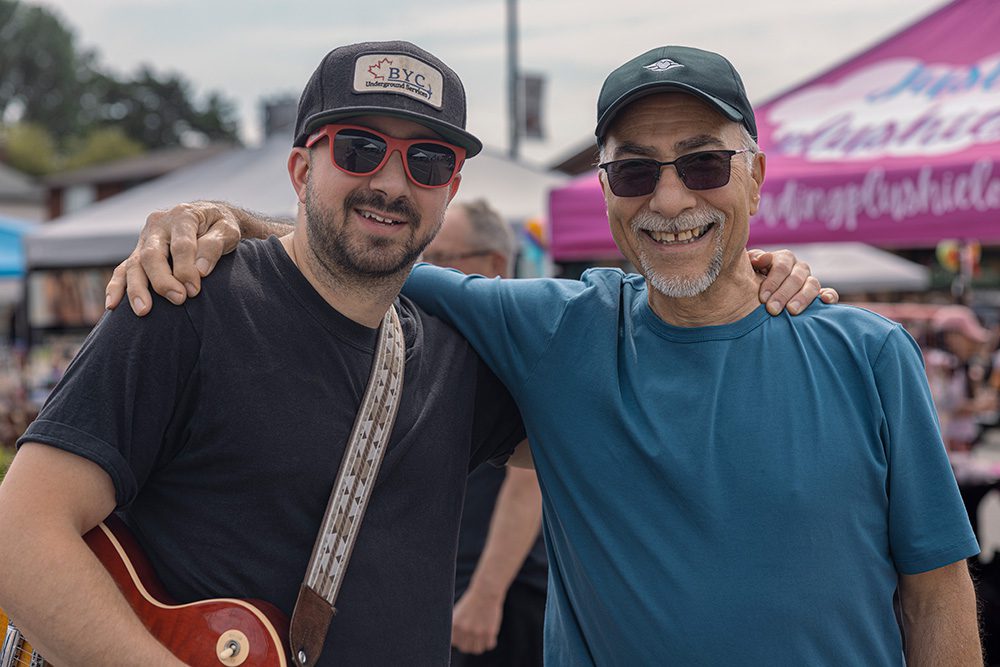 Two male musicians with acoustic guitar posing together at outdoor music festival