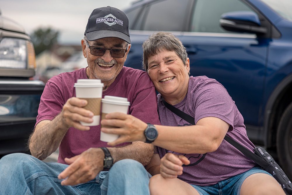 Couple in matching purple shirts toasting with coffee cups at outdoor festival