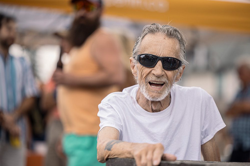 Senior man in sunglasses smiling broadly at outdoor community festival