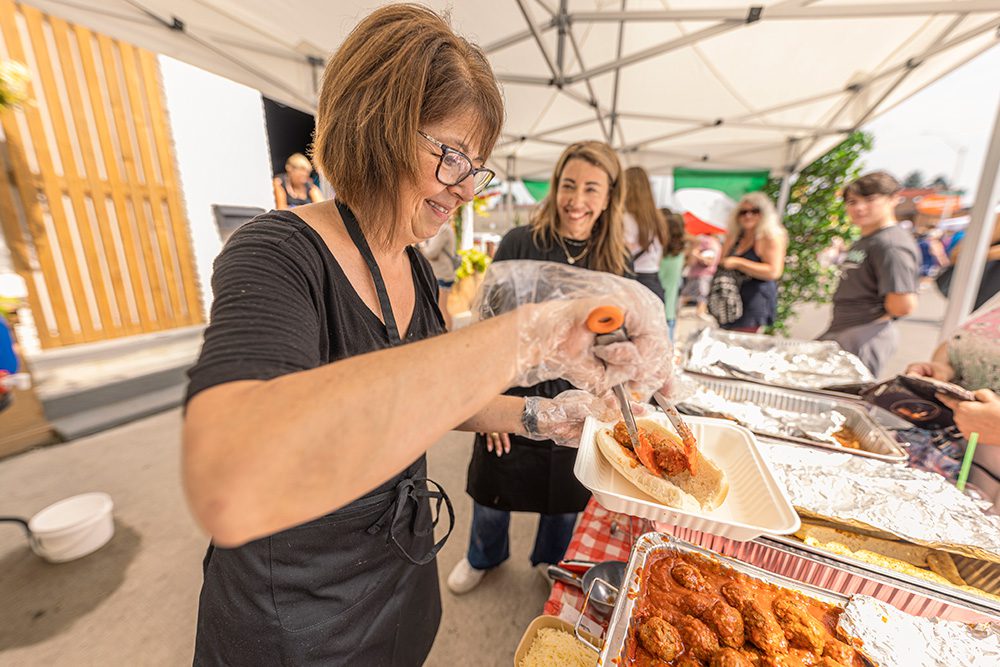 Volunteer serving food at outdoor festival tent with attendees waiting in line