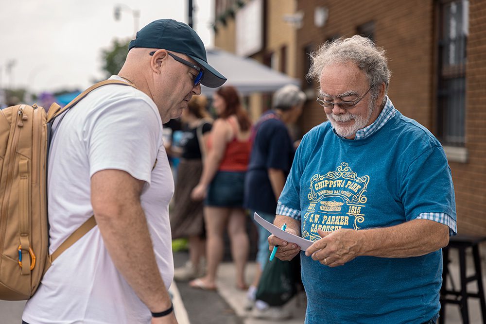 Two men discussing event map and schedule at outdoor community street fair